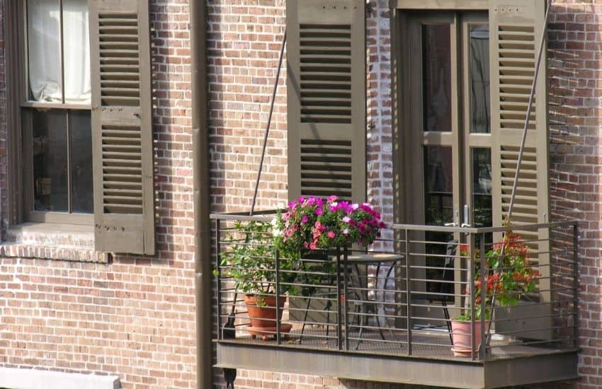 Small apartment balcony with flower boxes on the railing against a brick wall